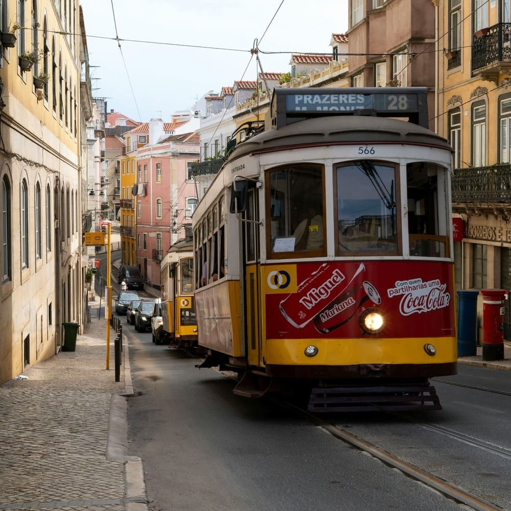 The famous Lisbon Tram 28 climbing through Lisbon’s historic hills, surrounded by colorful buildings and a vibrant city atmosphere.