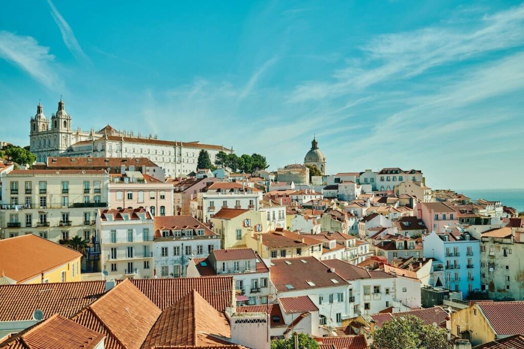Aerial view of Alfama in Lisbon, showing traditional red rooftops, narrow historic streets, and the Tagus River in the background, perfect for a Lisbon 1 Day Itinerary exploring the city.