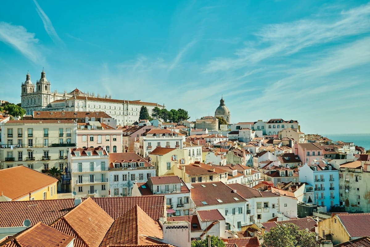 Aerial view of Alfama in Lisbon, showing traditional red rooftops, narrow historic streets, and the Tagus River in the background, perfect for a Lisbon 1 Day Itinerary exploring the city.