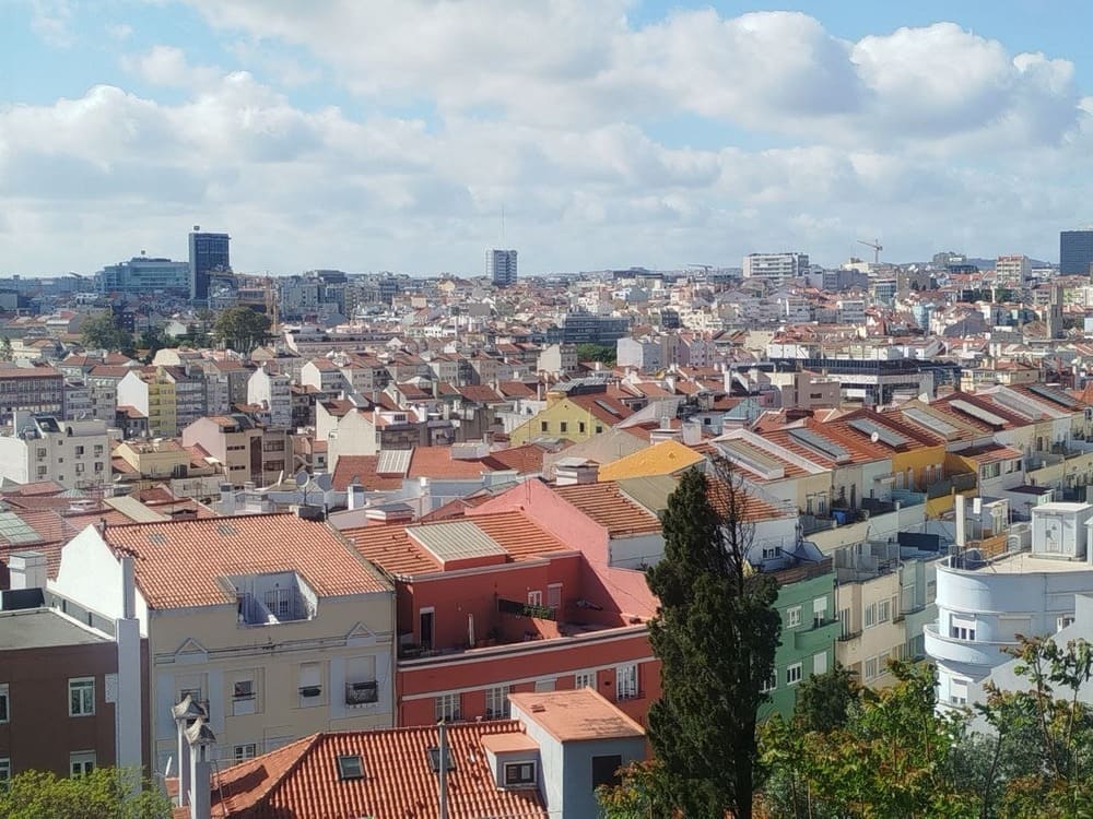 Panoramic view of Lisbon from the Monte Agudo viewpoint, showing city buildings and the open sky in the background.