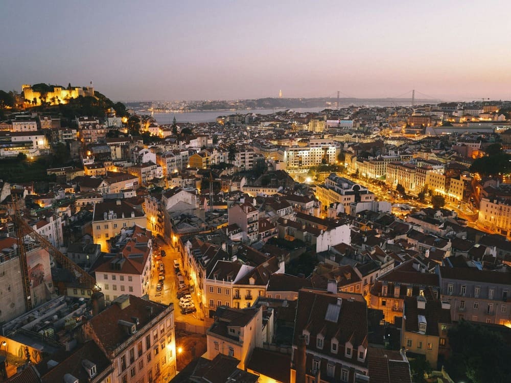 Aerial view of Lisbon at night, with illuminated streets, buildings, and the glow of the city’s nightlife.